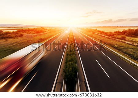 Highway in a strong back light at sunset with motion blurred truck landscape