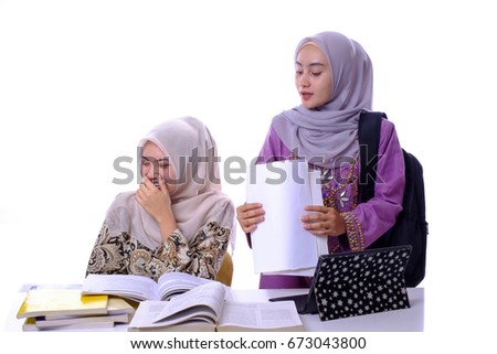 Elegant attractive Asian  female students  with hijab  studying together with mobile laptop and looking at text book content discussing how to do.