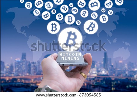 The hand holding a smartphone and the Bitcoin hologram on top blurred cityscape is backdrop. The concept of modern communication, smartphone, internet of things and financial.