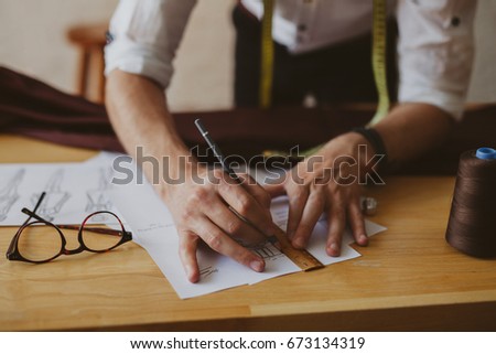 Tailor preparing new cloth drawing sketch with measurements on his working desk.