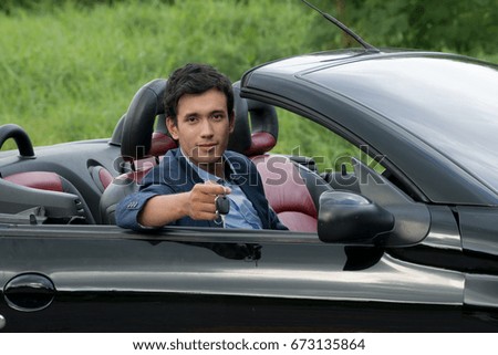 The business happy man holding and showing his convertible sport car keys in the garden, Age 20-30 years.Happy,Smiling man showing a new car key - car sale & rental business concept.Age 20-30 years.