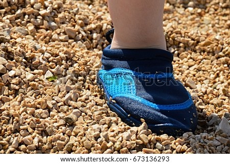 Foot of young boy on a stony beach wearing protective neoprene blue swimming shoes