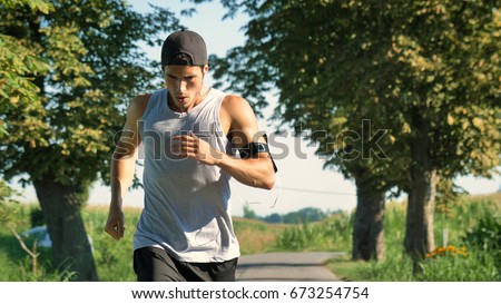 Portrait of a handsome young guy sportsman, holding a phone, smiling, wearing sports clothes, running outside. Concept: love sports, healthy lifestyle, be beautiful, muscles, happy, burn calories. Royalty-Free Stock Photo #673254754