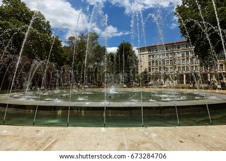 Classic urban fountain in the city square on a hot, sunny day. Classic urban fountain, streams and splashes of refreshing water. Fountain with a spray. VARNA, BULGARIA