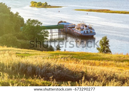 Loading grain from the elevator to the barge on the river in the summer at sunset on a clear day Royalty-Free Stock Photo #673290277