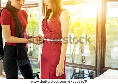 Young Asian female fashion designer working on garment on dressmaker model .Fashion designer measuring a dress work in studio.with female model
