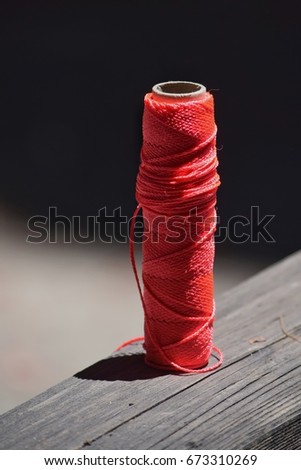 Still life of a spool of bright red kite string on a wooden railing. The beautiful light and shadow background makes this picture pop.
