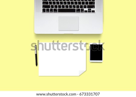 Top view of laptop with English keyboard and pen and blank white paper on yellow background