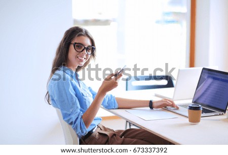 Beautiful young business woman sitting at office desk and holding cell phone