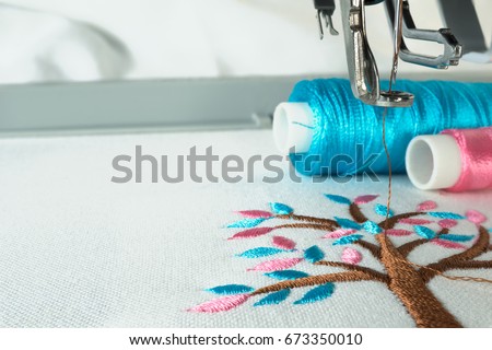 Picture of workspace in the embroidery machine close up look under the needle, lovely tree minimal style on background have two colorful thread cyan and pink.