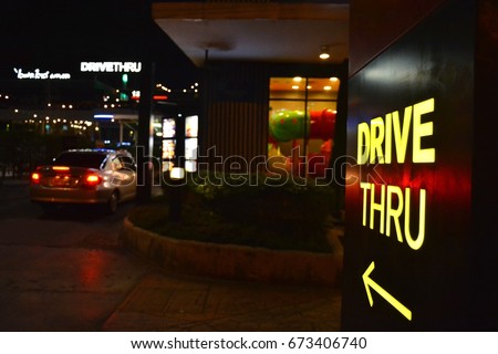 Yellow drive thru sign with an arrow pointer. A car drive into fast food restaurant in the late of night then order some food. Fast food store that open 24 hours selling burger, fried and nugget.