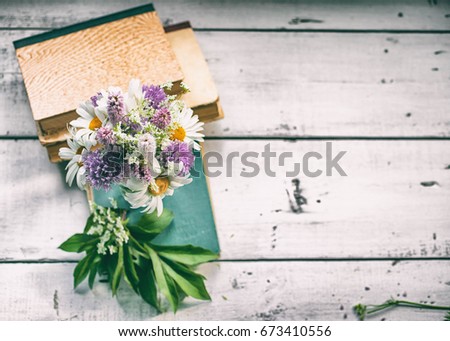 Vintage composition. Wild summer flowers and old books on a rustic wooden table. Vintage toning. Top view