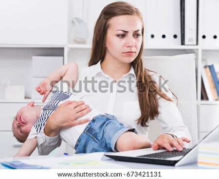 Female is working on laptop while kid naughty in office.