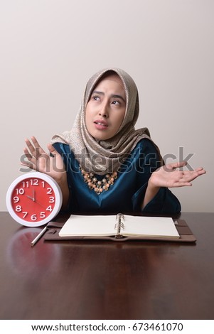 Young Muslim woman with book and alarm clock