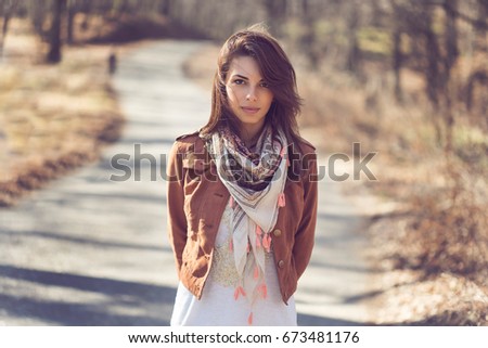 Portrait of a beautiful young brunette standing on the forest road in autumn