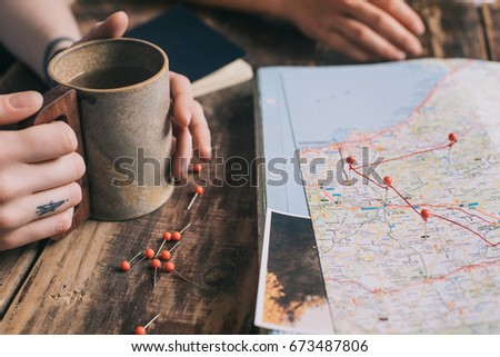 Two young girls explore paper map of Europe for new routes for summer trip. Students get inspired with photos of nature and planning their journey on dark wooden table with cups of tea, close up view
