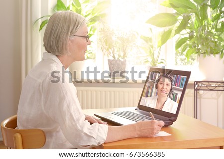 Senior woman in her sunny living room in front of a laptop making notes during watching an online advice video by a female therapist Royalty-Free Stock Photo #673566385