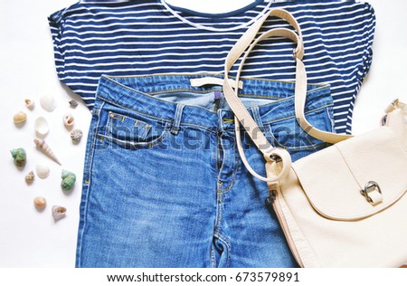 Striped female tshirt, fashionable blue jeans, beige bag and seashells. Summer women's wardrobe, relaxed clothes for traveling and recreation. Flat lay stock fashion photography