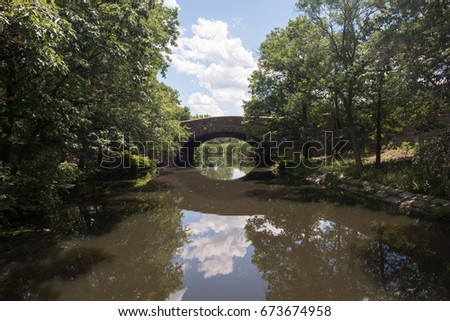 Lovely old, stone bridge, built in colonial times, in a quaint New England town, over a peaceful waterway that reflects a clear blue sky.
