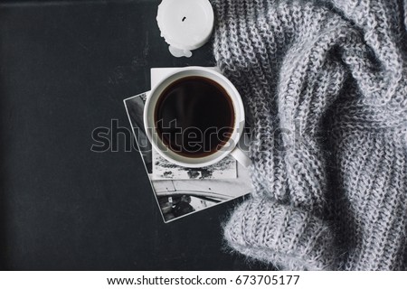 Winter cozy concept. Flatlay of gray knitted sweater, candle and coffee drink on black iron table. Warm weekend in cold weather.