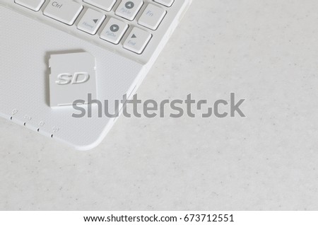 A compact SD memory card lies on a white netbook. The digital information storage device is ready for use. Concept of modern technologies