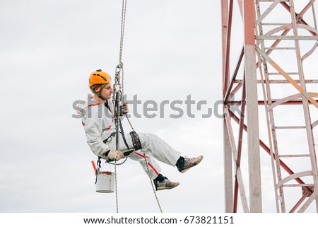 Industrial climber in helmet and uniform paints metal construction with paint roller. Professional Painter working on height. Risky job. Extreme occupation. Royalty-Free Stock Photo #673821151
