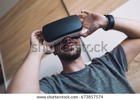 Young bearded man enjoying virtual reality at his home. Low angle view.
