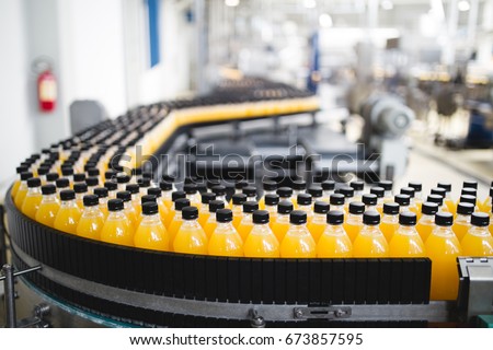 Industrial factory indoors and machinery. Robotic factory line for processing and bottling of soda and orange juice bottles. Selective focus. Short depth of field. Royalty-Free Stock Photo #673857595