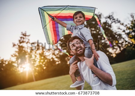 Handsome dad with his little cute sun are having fun with kite on green grassy lawn Royalty-Free Stock Photo #673873708