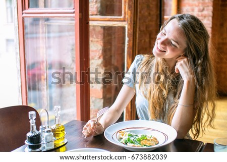 The portrait of fashion beautiful the brunette of the woman sending an air-kiss, sitting in cafe and lovely smiles, eats salad, positive emotions, the hipster an urban style.
