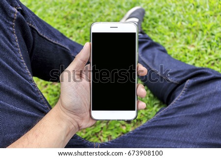 close-up hand  holding a phone sitting on green grass with soft-focus in the background, over light