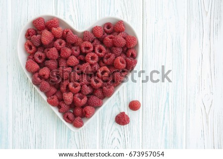 Raspberries in heart shaped plate on wooden background