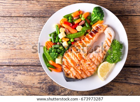 plate of grilled salmon steak with vegetables on wooden table, top view Royalty-Free Stock Photo #673973287