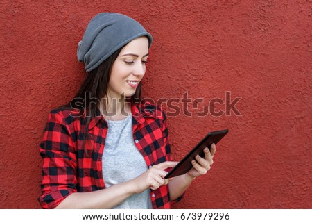 Young smiling girl using digital tablet outdoors, red wall in the background. Copy space
