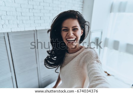Sincere smile. Self portrait of attractive young woman looking at camera and smiling while standing in the bedroom at home Royalty-Free Stock Photo #674034376