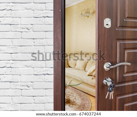 Half opened door, entrance to a living room. Welcome, privacy concept. Door lock with keys, white brick wall, modern interior design.
