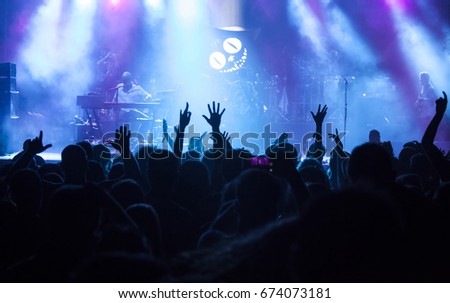 Photo of many people enjoying concert, crowd with raised up hands dancing in nightclub, audience applauding to musician band, night entertainment, music festival.