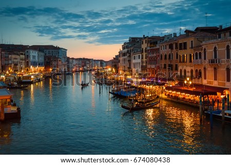Grand Canal with gondolas at night, Venice, Italy. Nightlife on embankments in summer. Skyline, scenic view and panorama of night Venice. Romantic water trip, tour, travel across Venice at dusk.