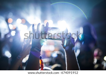 Woman in the crowd taking picture of stage at music festival. Hands up. Music and party concept.