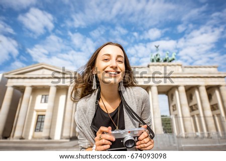 Portrait of a young smiling woman tourist standing with photo camera in front of the famous Brandenburg gates in Berlin