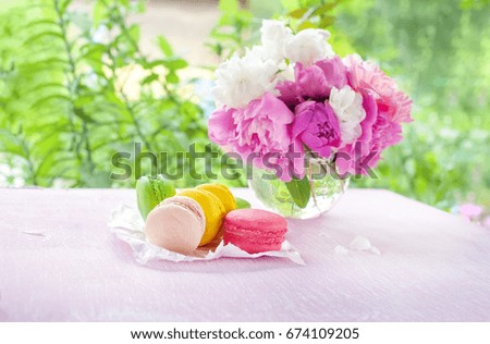 Cookies of macaroni yellow, red, green, and pink flowers on a background of a bouquet of peonies. The horizontal frame.
