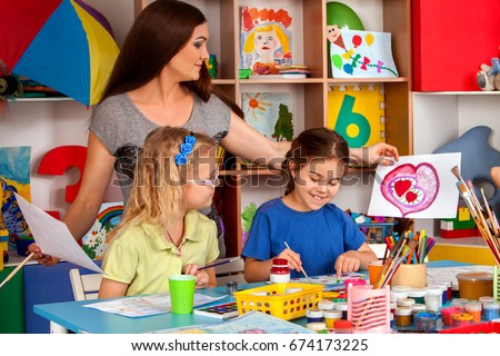 Craft lesson in primary school. Kindergarten teacher and small students work together. Girls at drawing lesson. Girl paints felt-tip pen picture in class. Children with teacher are preparing for an