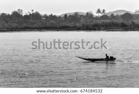 Black and white monochrome image of the boat sailing on Mekong river with forest and mountain on background

