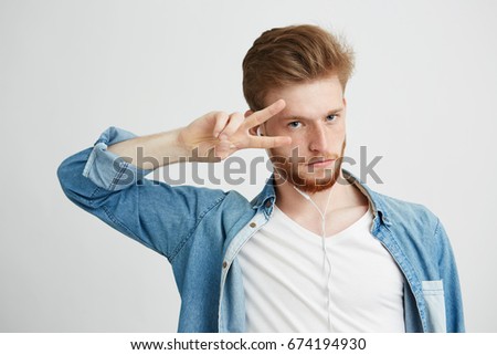 Young positive handsome man in headphones listening to music dancing showing peace over white background.