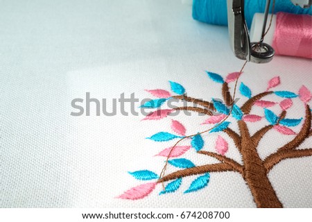Close up macro photo of small brown tree with cyan and pink leafs design on white fabric make with embroidery machine and  two threads on the background