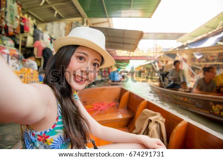 elegant attractive girl on river boat taking picture selfie and viewing floating market scene enjoying summer vacation during Thailand travel.