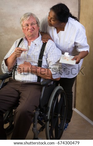 Grumpy old grandpa in nursing home receiving medication by a nurse