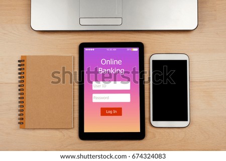 Digital tablet with Online Banking on screen with smartphone and notebook with laptop on wooden desk for Online Banking Payment Finance Concept, top view