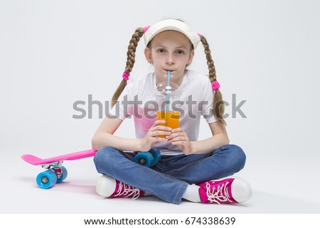 Kid Ideas and Concepts. Portrait of Pretty Caucasian Blond Girl wearing Visor Sitting on Floor with Cup of Juice and Drinking Through Straw. Horizontal Image
