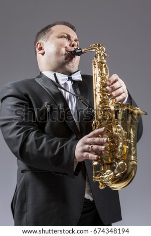 Music and Musicians Ideas and Concepts. Portrait of Caucasian Mature Expressive Saxophone Player Playing the Instrument Against White Background. Vertical Image Orientation